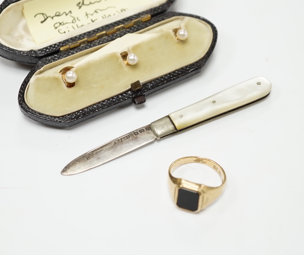 A 1960's 9ct gold and black onyx set signet ring, size O, gross weight 5.1 grams, a cased set of three yellow metal and cultured pearl set dress studs, a 9ct stick pin and a small mother of pearl handled silver fruit kni